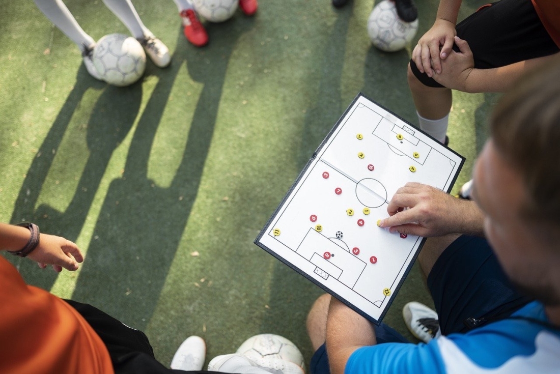 Coach erklärt Spielern Strategie auf dem Spielfeld - Ratgeber Fußballmanagement Studium