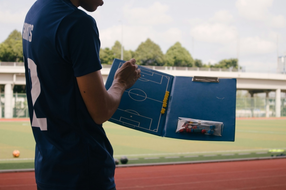 Trainer am Rande des Spielfeldes mit einer Tafel - Ratgeber Fußballmanagement Studium