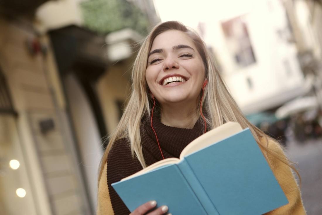 Lächelndes Mädchen mit Kopfhörern und Notizbuch in der Hand - Ratgeber Studieren in Spanien: Campus M University