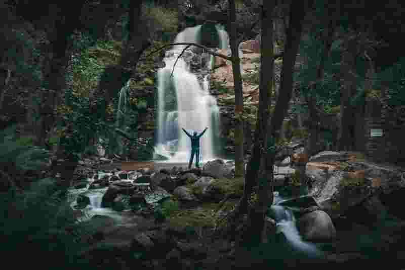 Mensch vor Wasserfall in tropischem Wald - Ratgeber Studium im Tourismus: Campus M University.