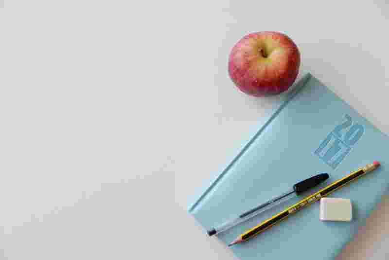 Notizbuch auf einem Schreibtisch mit Stiften und Apfel - Ratgeber Studium zum Ernährungsberater: Campus M University.