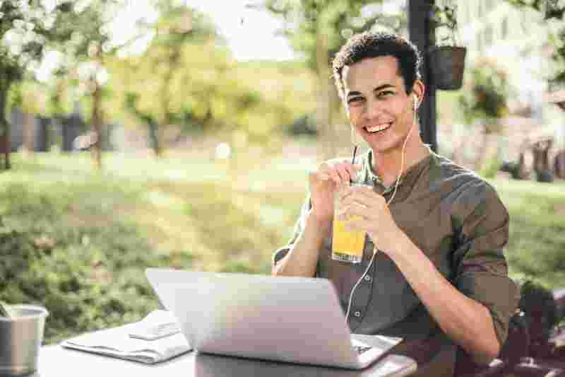 Glücklicher Student, der mit Laptop und Saft im Park Sitzt - Ratgeber Studium zum Ernährungsberater: Campus M University.