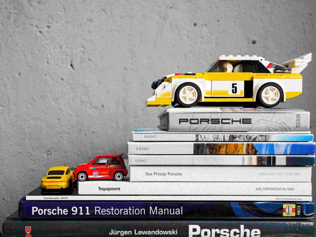 Kleine Modellautos auf einem Stapel Bücher über Porsche auf einem Tisch - Symbolbild für das Automobilbusiness.