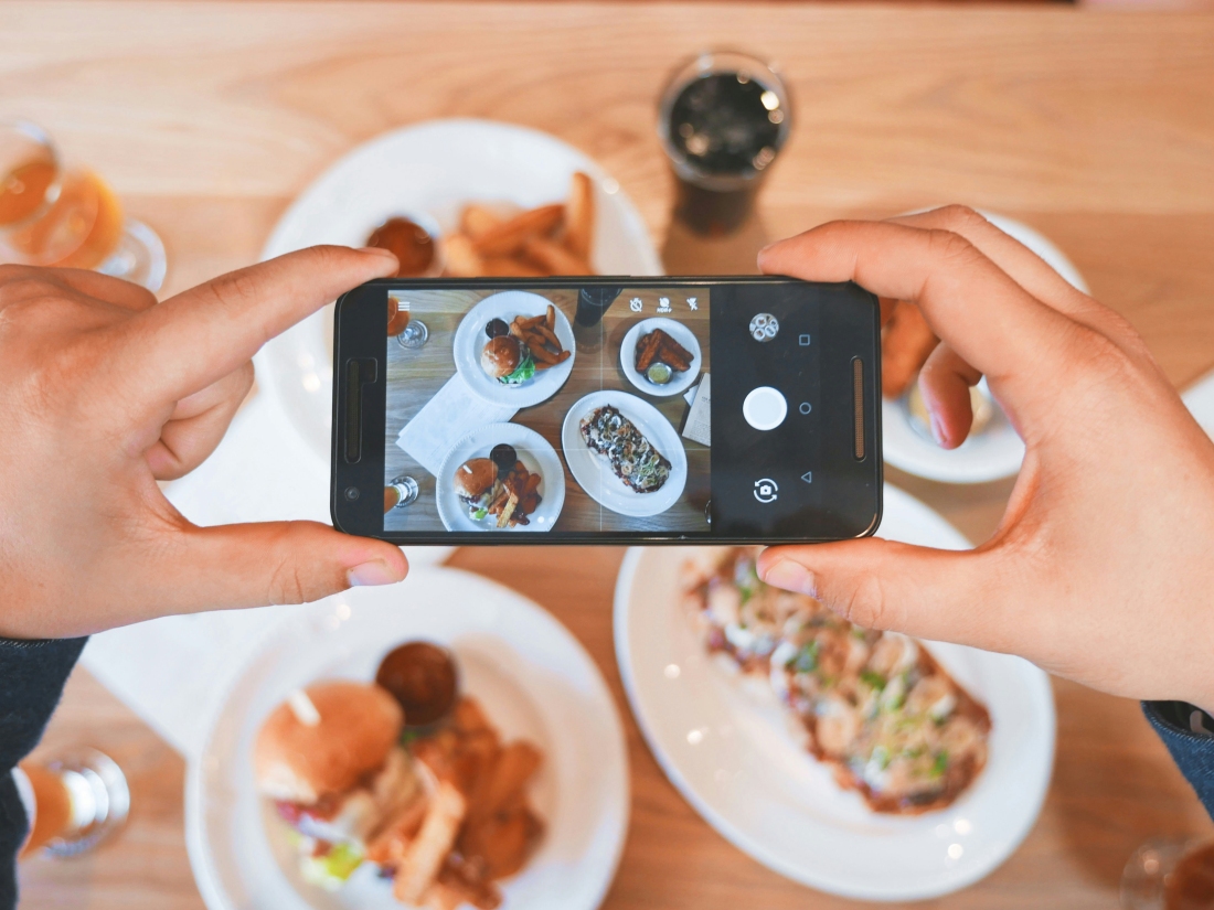 Gehaltenes Handy, mit dem gerade ein ausgiebiges schönes Frühstück fotografiert wird - Ratgeber Social Media Studium: Campus M University.