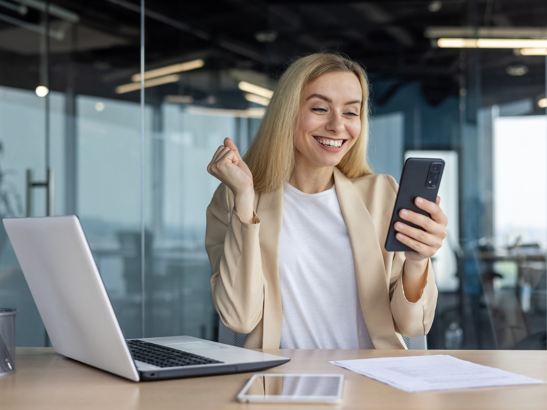 Arbeitende Frau freut sich über eine Nachricht auf ihrem Handy - Ratgeber Social Media Studium: Campus M University.