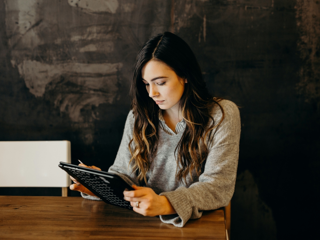 Lachende Frau mit IPad an einem Tisch - Ratgeber Studium im Tourismus: Campus M University.