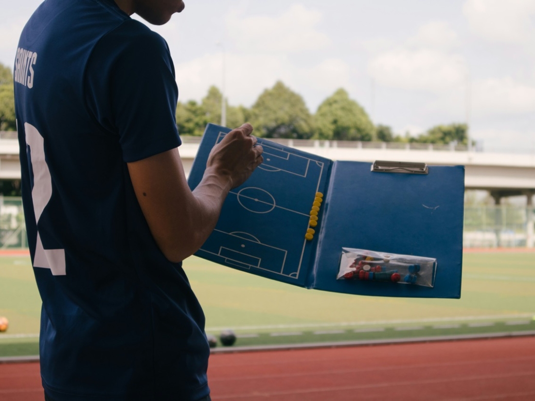 Trainer hält Tafel mit Fußballfeld und zeigt etwas - Ratgeber Sportpsychologie Studium Campus M University