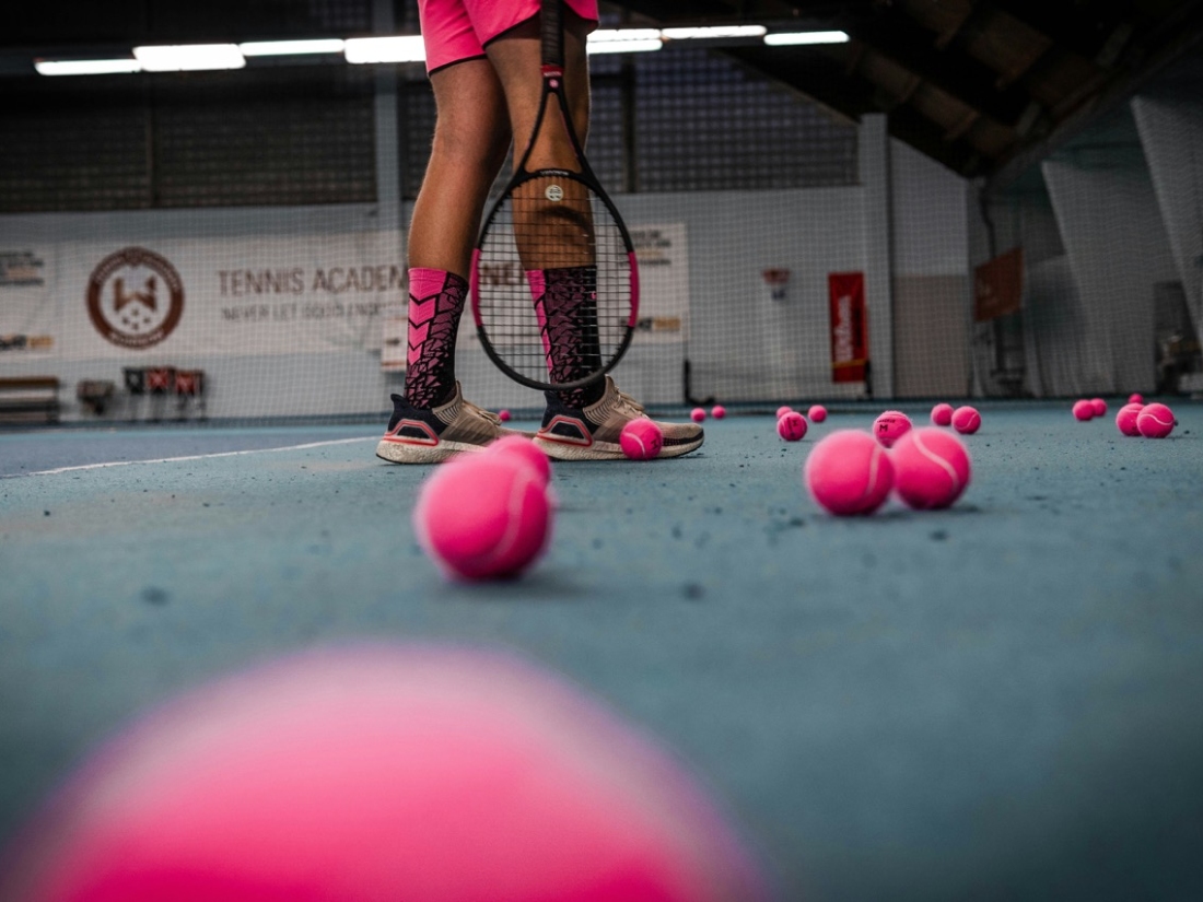 Beine einer Tennisspielerin und pinke Bälle am Platz - Ratgeber Sportpsychologie Studium Campus M University