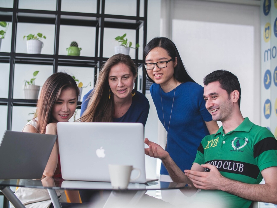 Vier lachende Studierende vor einem Laptop - Ratgeber Studium im Tourismus: Campus M University.